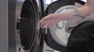 Man puts laundry in the washing machine drum and closes the door