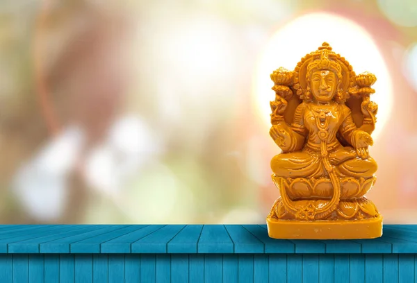 木製のテーブルの上に茶色の木に刻まれたMahalakshmiの像は 頭の後ろに強力な光を持つ自然なボケの背景を持っています — ストック写真