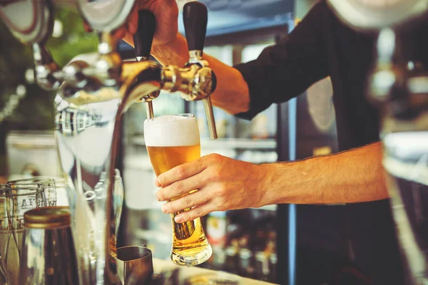 Close-up of young bartender pouring beer while standing at the bar counter.