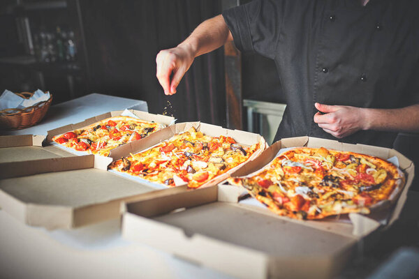 Closeup hand of chef baker in white uniform cutting pizza at kitchen.