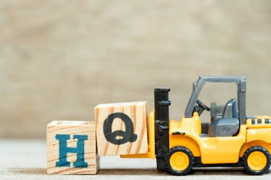 Oyuncak forklift harf bloğu Q 'yu ahşap arkaplan üzerindeki HQ (karargahın kısaltması) kelimesinin tamamlanması için tut