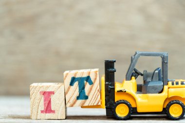 Oyuncak forklift harf bloğu T 'yi ahşap arkaplan üzerine bilgi teknolojisinin kısaltması olarak tamamlamak için