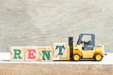 Oyuncak forklift harf bloğunu ahşap arkaplanda kelime kirasını tamamlamak için tut
