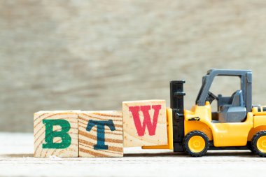 Toy forklift harf bloğu W 'yi tahta arkaplan üzerindeki BTW (bu arada kısaltması) sözcüğünü tamamlamak için