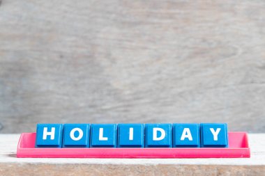 Tile alphabet letter with word holiday in red color rack on wood background