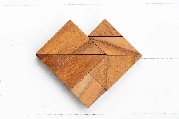Wood tangram puzzle in heart shape on white wood background
