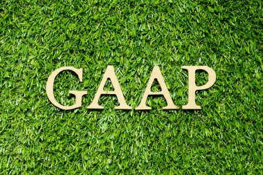 Wood alphabet letter in word GAAP (Abbreviation of Generally accepted accounting principles) on green grass background
