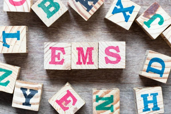 Alphabet letter block in word EMS (abbreviation of emergency medical services or express mail service) and another letter on wood background