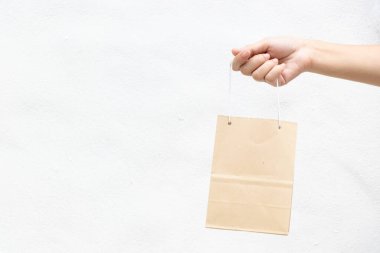 Hand of business woman hold brown paper shopping bag on white concrete background