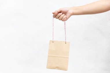 Hand of business woman hold brown paper shopping bag on white concrete background