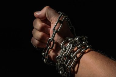 Metal zincirlerle zincirlenmiş insan eli siyah arka planda izole edilmiş.
