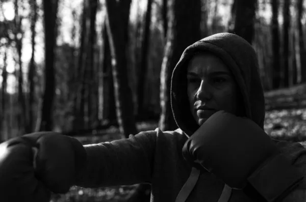身着运动服头戴红色拳击手套头罩的年轻漂亮女子拳击手在大自然的森林里训练 — 图库照片