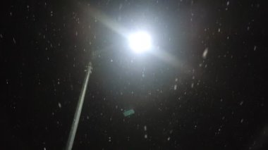 Kar yağışı sırasında sokak lambaları kar tanelerini aydınlatıyor.