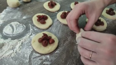 Hands of a woman cook who sculpts traditional donuts with cherries from the dough, on the kitchen table with flour