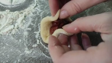 Hands of a woman cook who sculpts traditional donuts with cherries from the dough, on the kitchen table with flour