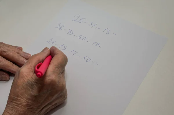 高齢の女性の手は紙にペンで数字を書きます — ストック写真