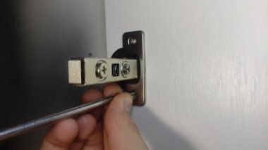 The furniture maker installs furniture hinges in the closet, tightening the screw with a screwdriver