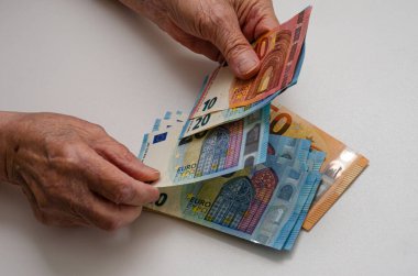 Avro banknotunu tutan yaşlı kadın, beyaz arka planda izole edilmiş parayı tutuyor