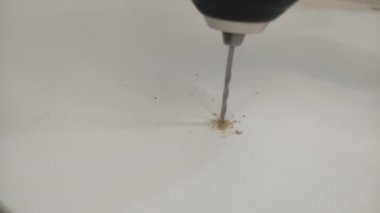 The master drills four holes in a wooden plate with a drill