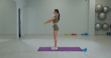 Sportive brunette girl performs raising her arms in front of her