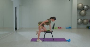 Sportive brunette girl performs extension of right arm in an incline