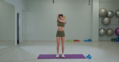 Athletic girl performs french press with dumbbell from behind head