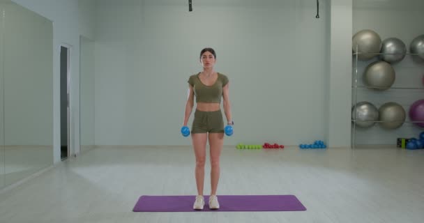 Athletic shape brunette girl performs flexion of arms for biceps alternately — Videoclip de stoc
