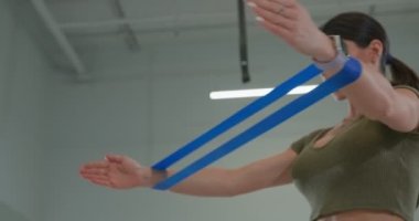 Athletic brunette girl performs a spread of arms with elastic band