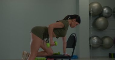 Athletic brunette girl performs extension of her arms on triceps in an incline