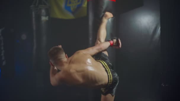 Un boxeador hace una serie de golpes en un saco de boxeo usando sus brazos y piernas — Vídeo de stock