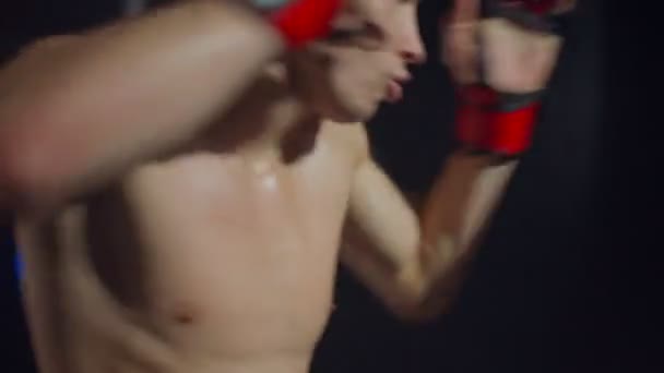 Боксер робить серію ударів по мішку, використовуючи руки і ноги — стокове відео