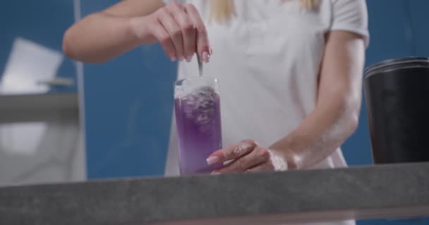 La mano femenina agita bsaa de color púrpura en un vaso de agua — Vídeos de Stock
