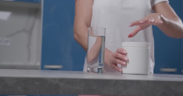 Uma mão das mulheres abre um frasco branco, derrama bcaa em um copo e agita-o. — Vídeo de Stock