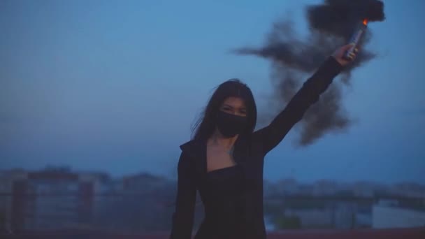Menina em máscara acenando bomba de fumaça preta no telhado — Vídeo de Stock
