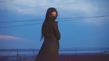 Şeffaf elbiseli ve maskeli kız çatıdaki kameraya poz veriyor.