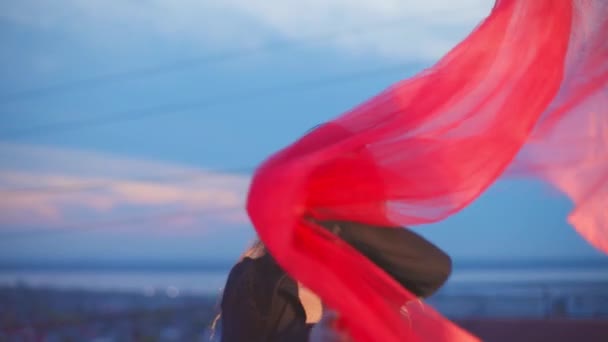 Dziewczyna w masce pozuje z czerwoną przezroczystą tkaniną na dachu — Wideo stockowe
