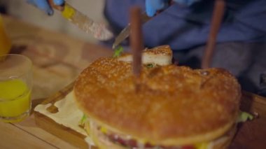 Tek kullanımlık eldivenli bir erkek eli sulu bir burgeri keser.