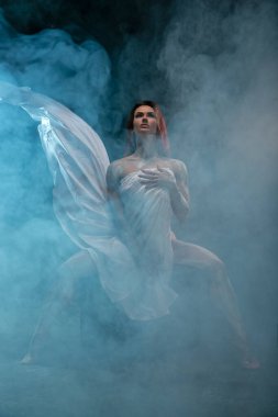 Kızıl saçlı kız, stüdyoda poz veren antika bir heykel gibi kendini beyaz kumaşla kaplıyor.