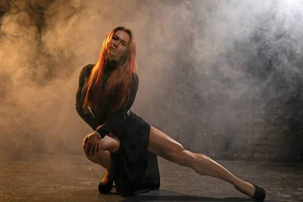 Atraente menina de cabelos vermelhos em vestido preto demonstra pernas atléticas — Fotografia de Stock