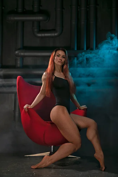 Bright girl with sexy legs posing in a red chair — Stok fotoğraf