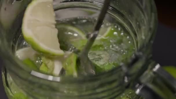 A long cocktail spoon stirs the mojito in a jug — Vídeo de stock
