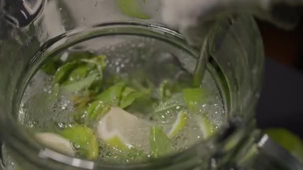 A long cocktail spoon stirs the mojito in a jug — Stock video