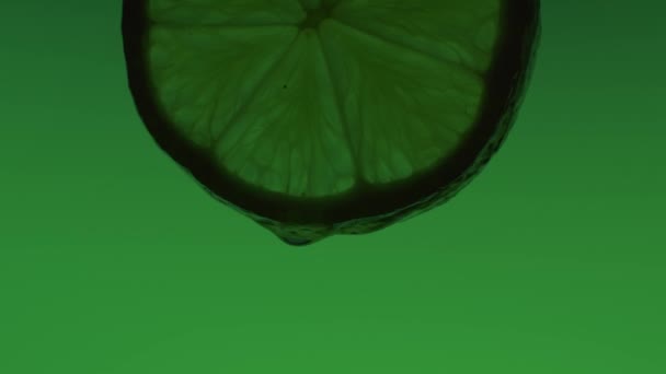 Drops of water flow down a slice of green lime — Vídeo de stock