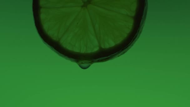 Drops of water flow down a slice of green lime — Stok Video