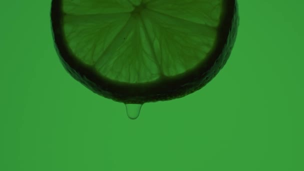 Drops of water flow down a slice of green lime — Vídeo de stock