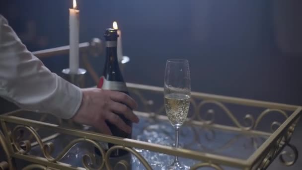 Een man opent een fles champagne en giet champagne in een glas. — Stockvideo