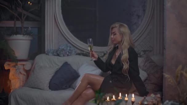 Blond kvinna dricker ett glas champagne på soffan — Stockvideo