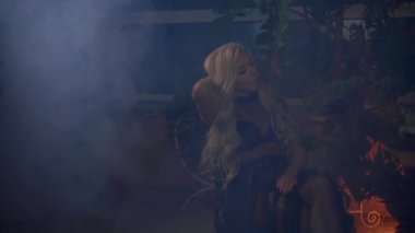 Sarışın kadın, galeride saçına sisli bitkilerle dokunuyor.