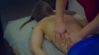 Kadın bir masörün elleri hızla yoğurur ve kadın bir hastanın sırtını ovar.