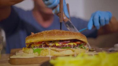 Yetişkin, kel bir adam büyük, sulu bir burgeri birkaç bıçakla keser.